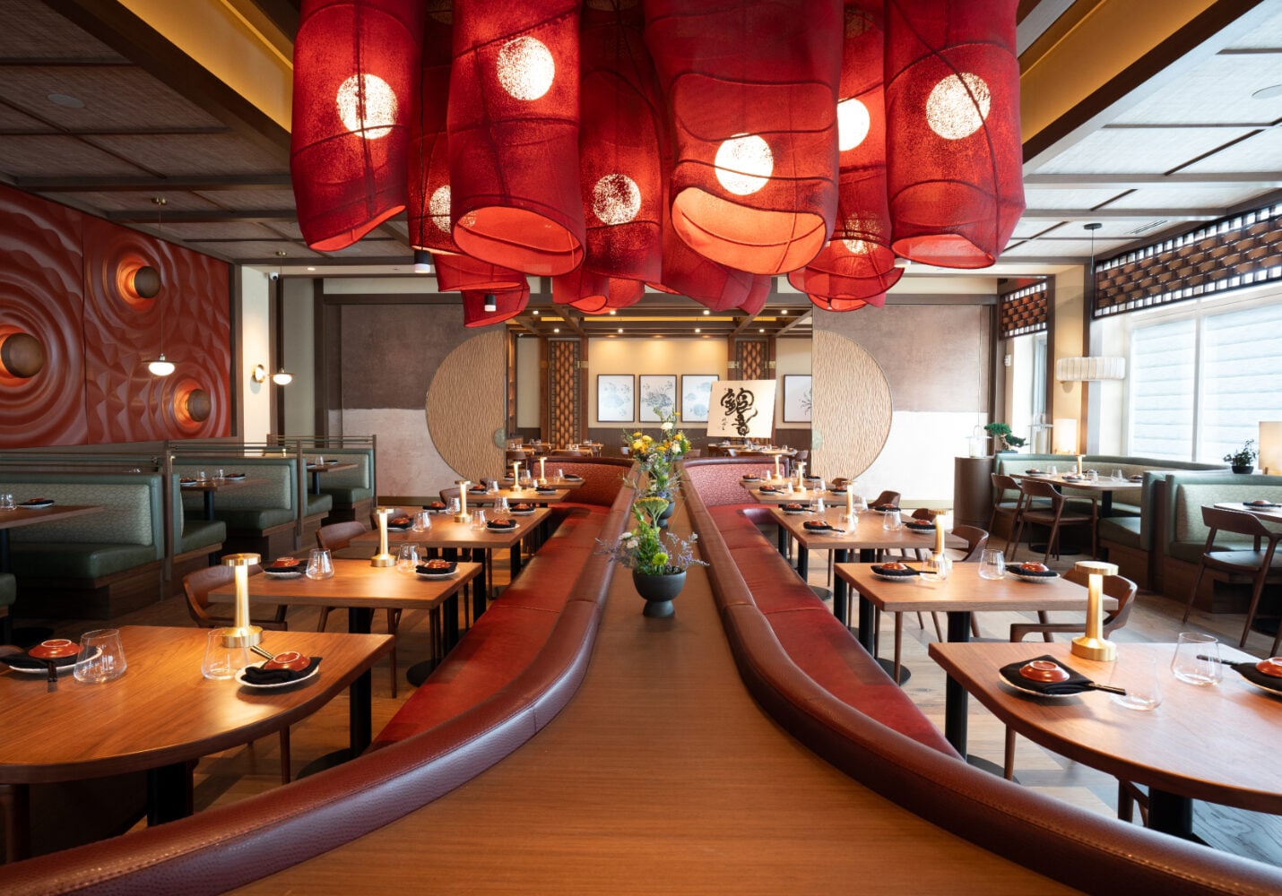 Restaurant interior with wood tables, booths, and large red fabric pendant lights hanging from the ceiling.