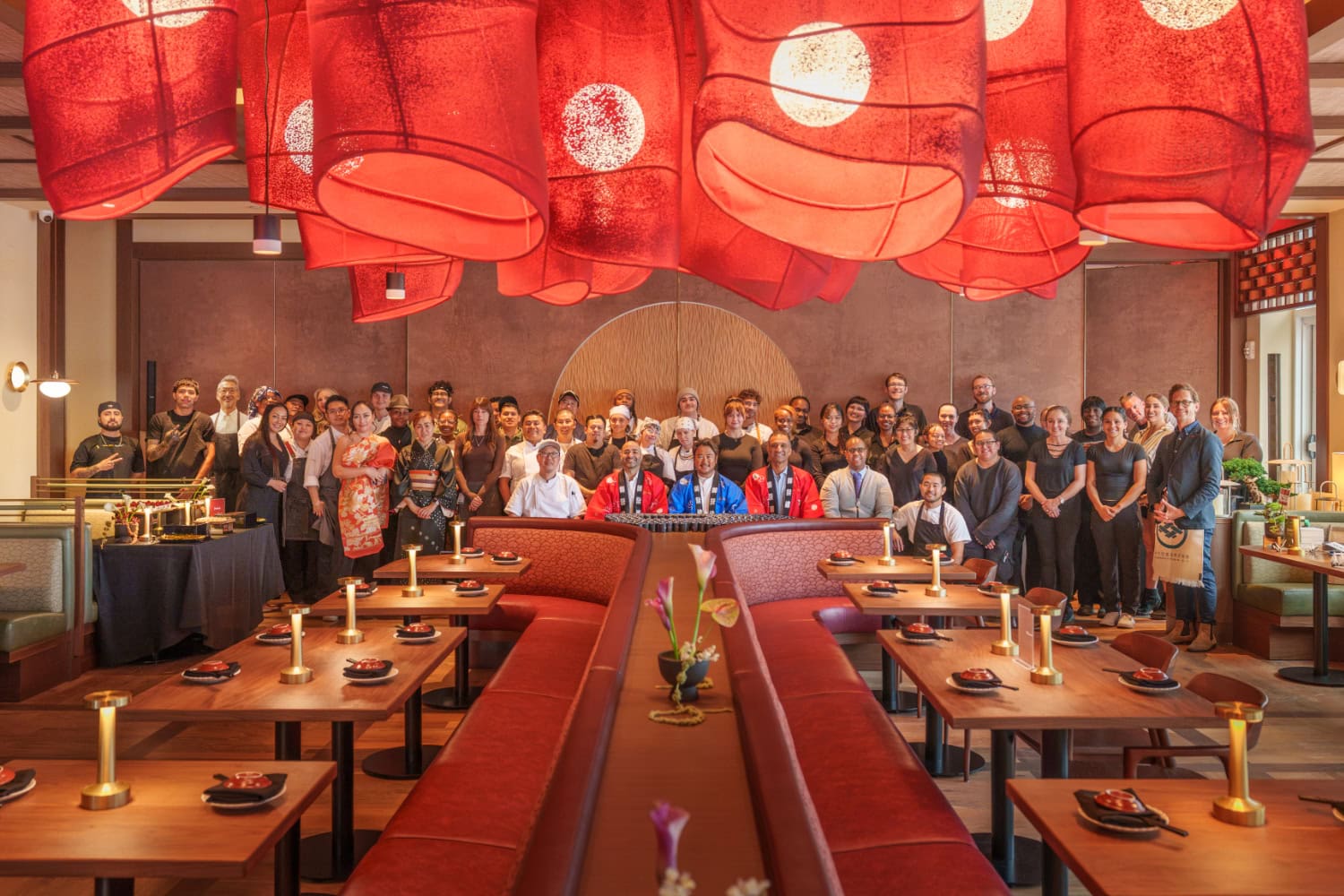 A large group of restaurant staff posing for a photo in a dining room under numerous red paper lanterns.